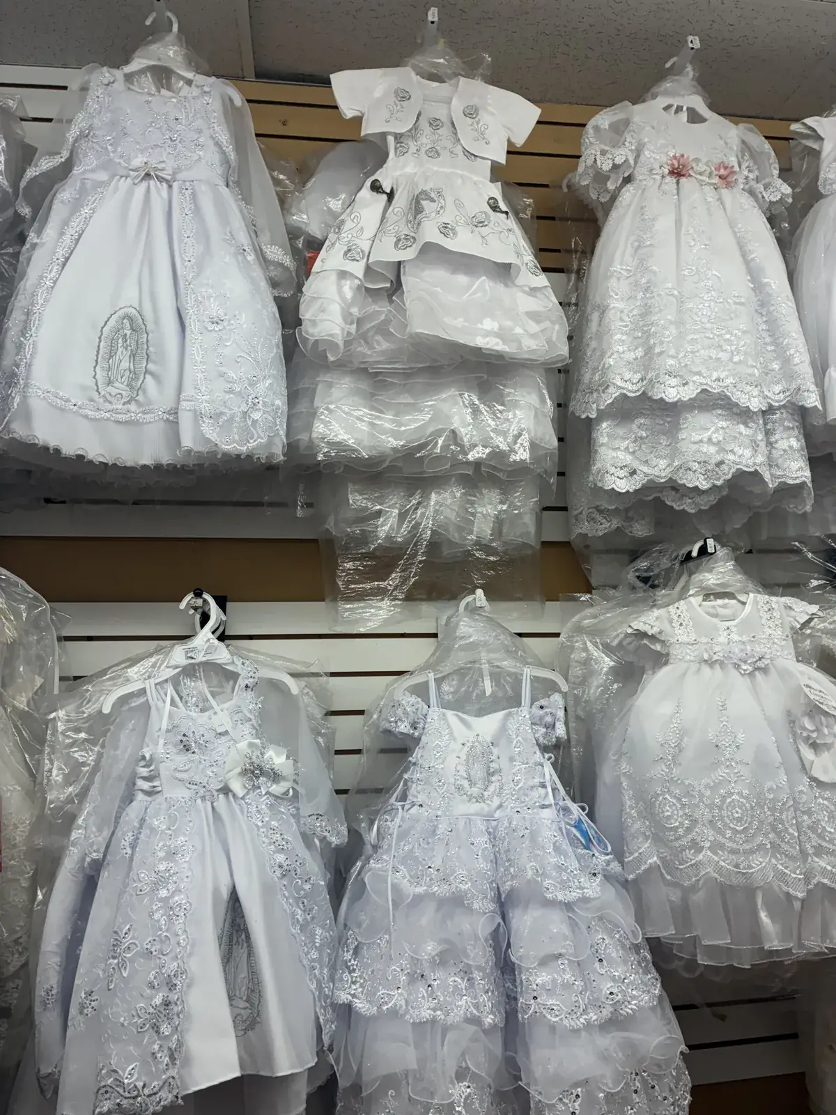 Lace baptism dresses with bows on display at Yessenia’s Fashion